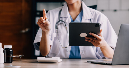 Concerned young female Caucasian doctor in white medical uniform sit at desk in hospital work on laptop, focused woman nurse or GP busy fill anamnesis on computer gadget, medicine, technology concept - obrazy, fototapety, plakaty