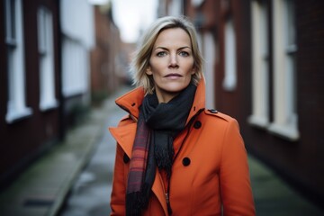 Beautiful blonde woman in an orange coat and scarf on a city street