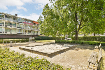 an empty bench in the middle of a park with trees and buildings in the background on a bright sunny day