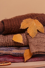 Pile of knitted wool sweaters with autumn dry leaves. Winter autumn cozy season concept.