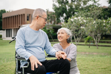 Asian Senior couple sitting in wheelchairs taking care of each other.in romantic time They laughing and smiling while sitting outdoor in park..