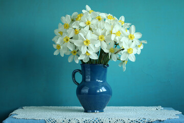 bouquet of white daffodils in a jug on a blue background.