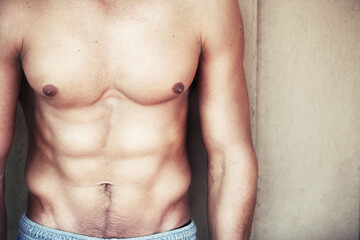 Naklejka premium Body, closeup and fitness man with abs, muscle or workout motivation on wall background. Chest, stomach and zoom on topless male model pose with muscular torso, pride and training, goals or results