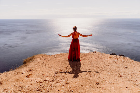 Woman red dress sea. posing on a rocky outcrop high above the sea. Girl on the nature on blue sky background. Fashion photo.