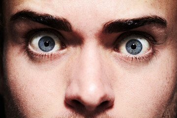 Closeup, face or eyes of shocked person with fear, terror and anxiety for schizophrenia or mental health. Man, stress or crazy looking with addiction, user and psychosis for insomnia, emotion or risk