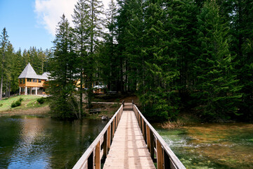 Wooden bridge across the lake to a house on the shore in a spruce forest