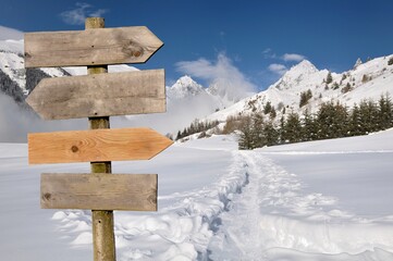 wooden directional post sign with arrow in  front of snowy mountain landscape