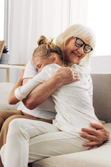Family hugging home sofa happy couch girl love child granddaughter grandmother - obrazy, fototapety, plakaty