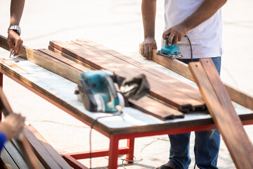 Selective focus to carpenter's hands smoothing a wooden surface with an electric planer. - obrazy, fototapety, plakaty
