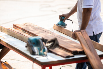 Selective focus to carpenter's hands smoothing a wooden surface with an electric planer.