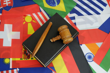 International laws problems. Broken judge gavel and legal book on background of many national flags.