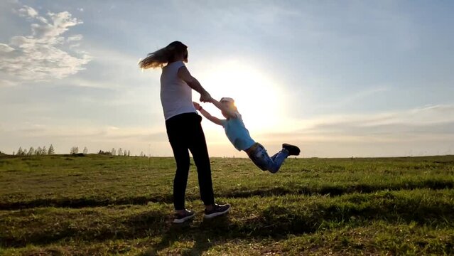 Happy mom is playing with the child in the sunset sun, they are circling around themselves
