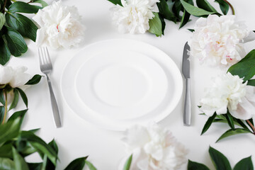 Festive table setting with white plate, cutlery and peonies on white table