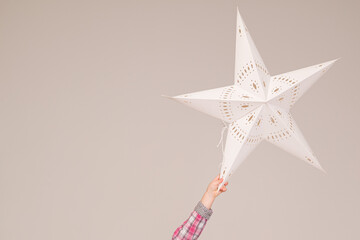 Closeup of A little girl's with a large paper Christmas star on a gray background. Christmas concept