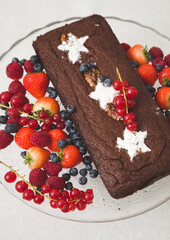 Chocolate brownie cake with fresh blueberries,  raspberries, strawberries, red currant and white stars made of powdered sugar. Homemade cake decorated with fruit. Festive concept