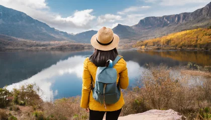 Keuken spatwand met foto Rear view of a stylish girl, with a backpack, a hat and a yellow jacket, looking at the view of the mountains and the lake while relaxing in the autumn nature. Travel concept. © Beste stock