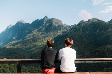 Fototapeta na wymiar Rear view image of two male traveler sitting and looking at a beautiful mountain,sky field and nature view