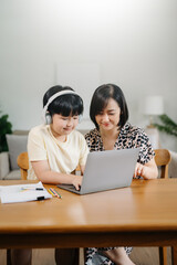 Homeschool Asian young little boy learning online and does homework by using computer and tablet with mother help, teach and encourage. son smile to study at home together with mom