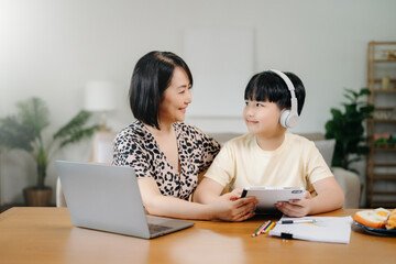 Homeschool Asian young little boy learning online and does homework by using computer and tablet...