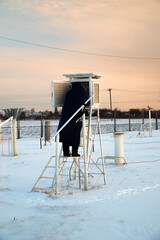 Human in winter in the evening maintains and takes readings from surveillance instruments at a weather station.