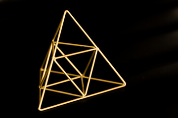 Shiny decorative golden pyramid on a black background. Space for text, concept, style