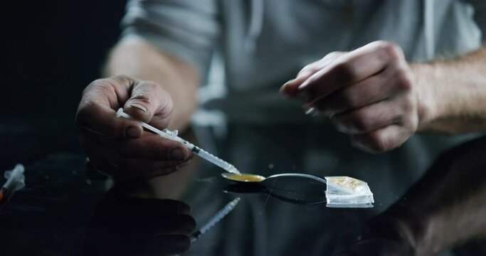 Hands, drugs and heroin with an addict closeup on a dark background to inject narcotics using a syringe. Depression, drug abuse and a spoon to melt an opioid for injection with a needle to get high