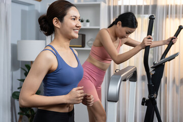 Fototapeta na wymiar Energetic and strong athletic asian woman running on elliptical running machine at home with workout buddy or trainer. Pursuit of fit physique and commitment to healthy lifestyle. Vigorous