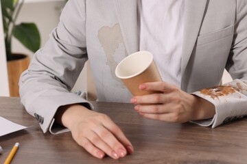 Woman showing stain from coffee on her jacket at wooden table indoors, closeup