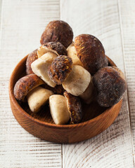 Frozen whole porcini mushrooms in a wooden bowl on a white background. Mushrooms, frozen foods.