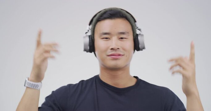 Asian man, headphones and dance to music for student wellness, streaming service and kpop song in studio. Young Korean person with audio, electronics and listening with energy on a white background