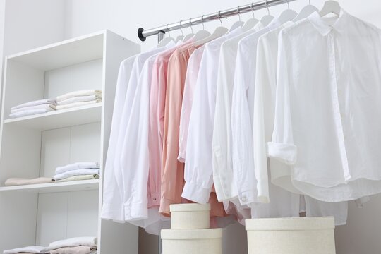 Wardrobe organization. Rack with different stylish clothes, shelving unit and boxes near white wall