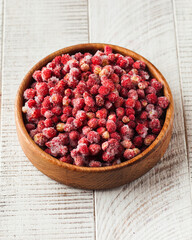 Frozen wild strawberries in a wooden bowl on a white wooden background. Berries, frozen foods.