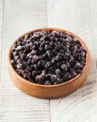 Frozen black currant in a wooden bowl on a white wooden background. Berries, frozen foods.