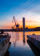 Gothenburg, Sweden - May 29, 2023: Large lifting crane in Gothenburg harbor during dusk. The sky is blue and orange. Next to it stands Karlatornet - the tallest skyscraper in Gothenburg