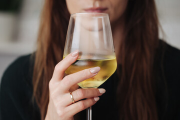 Woman drinking wine. White wine drinking. Wine glass in hand. Girl in woolen sweater. Cozy winter alcohol background. Female hand holding wine glass. Winter season clothing. Shallow depth of field.