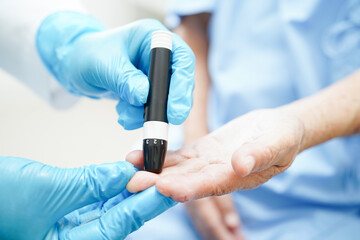 Obraz na płótnie Canvas Asian doctor using lancet pen on senior patient finger for check sample blood sugar level to treatment diabetes..