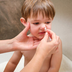 The mother is removing snot from her baby boy's nose using a cotton swab in the bathroom. Kid aged two years (two-year-old boy)