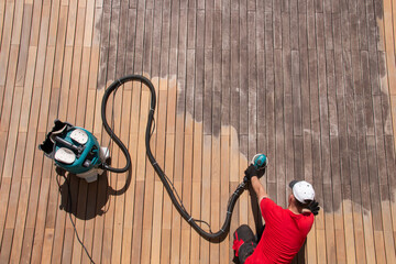 Wood deck repair top view, gray ipe decking boards maintenance, man sanding with orbital power...