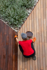 A worker painting wooden deck with protective decking oil bucket top view