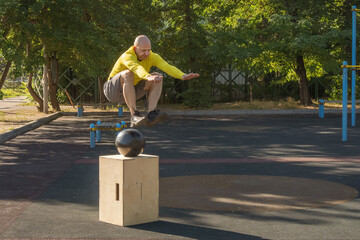 Man jumps over a wooden box while exercising at an outdoor sports ground. Healthy lifestyle