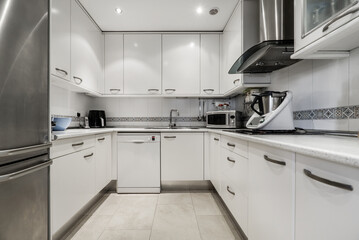 Fototapeta premium Furnished U-shaped kitchen with white cabinets and integrated stainless steel appliances and small appliances on the countertop