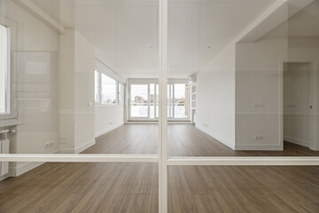 Fototapeta na wymiar Panoramic view of a living room with wooden floors and access to a terrace of an apartment through a glass and white painted metal screen.