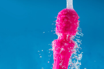 Pink vibrator under running water on a blue background. Sex toy hygiene concept.