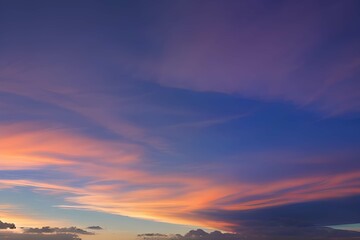 Fototapeta premium 夕暮れの色彩：オレンジ、青、紫のグラデーションが広がる空と、暗くて細い雲が交差する、低角度から見上げた夕暮れの風景