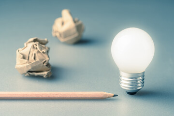 Glowing light bulb with pencil and crumpled paper balls, inspiration, start writing, writing tips - obrazy, fototapety, plakaty