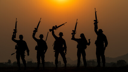 Fototapeta na wymiar silhouette group of special forces sodiers standing and holding gun over the sunset and colorful orange sky background