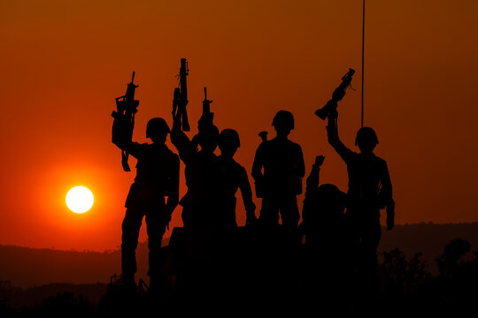 silhouette group of special forces sodiers standing and sit holding gun on cannon tank with over the sunset and colorful orange sky background,