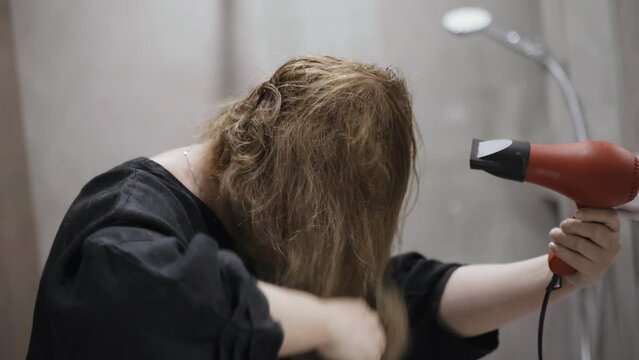 A woman dries her hair with a hairdryer in the bathroom. Close-up. Concept of a well-groomed and beautiful woman.