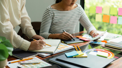 Two creative graphic designers hold color swatches to discussing and sketching to designing project