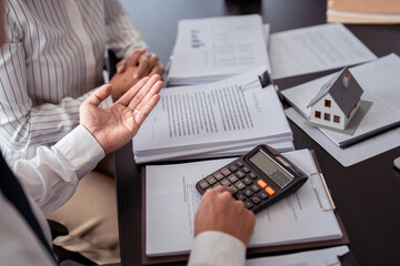 Businessman real estate seller calculating about property investment and showing statistic on calculator while discuss to explaining terms data of home sales contract and home insurance for customer